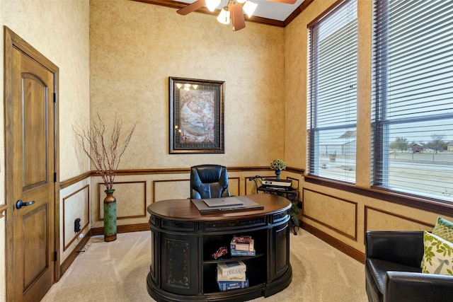 office area featuring light colored carpet, a decorative wall, ornamental molding, wainscoting, and ceiling fan