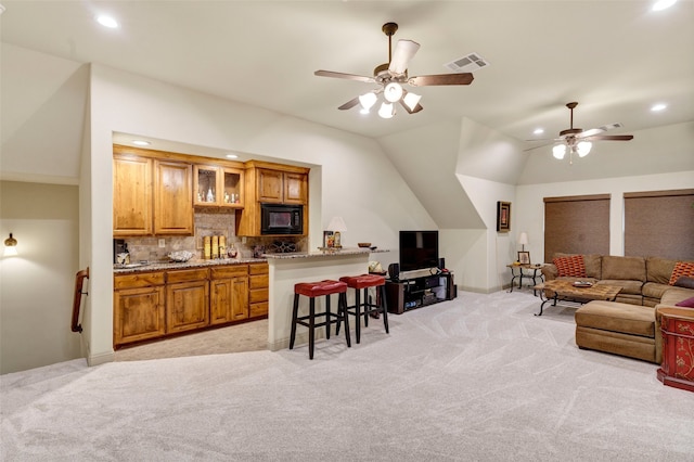 interior space featuring a breakfast bar, brown cabinets, visible vents, light colored carpet, and black microwave