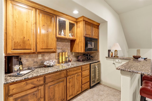 kitchen with stone countertops, black microwave, brown cabinetry, and a sink