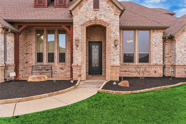 view of exterior entry with brick siding, stone siding, and roof with shingles