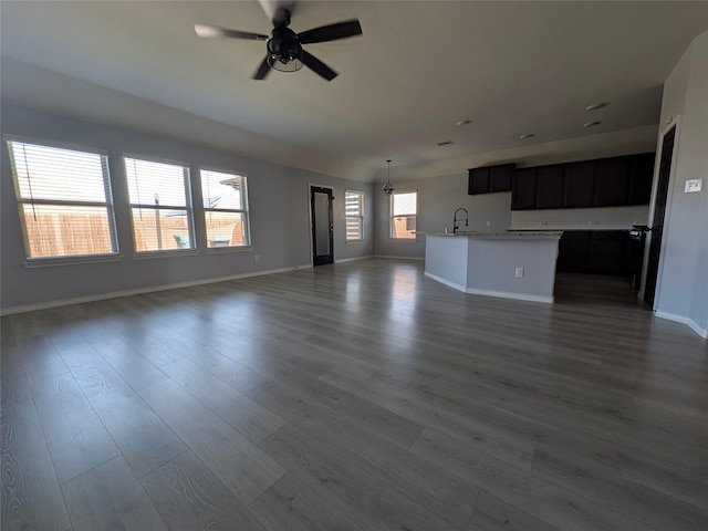 unfurnished living room featuring ceiling fan, baseboards, dark wood-type flooring, and a sink