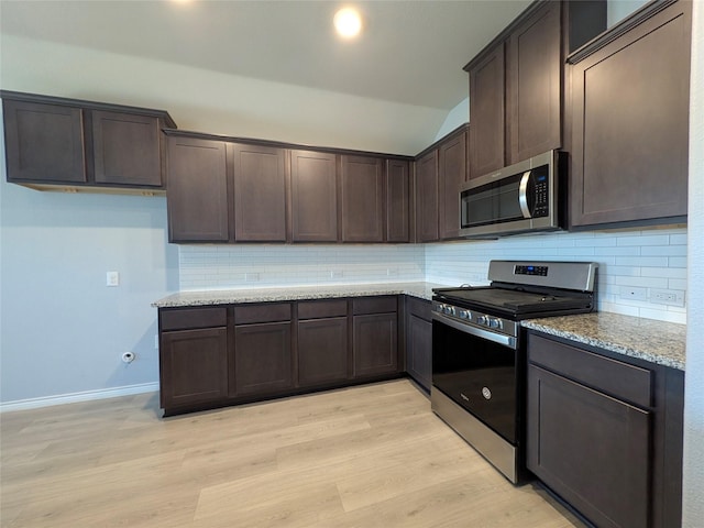 kitchen with appliances with stainless steel finishes, light wood-style floors, dark brown cabinets, and light stone countertops