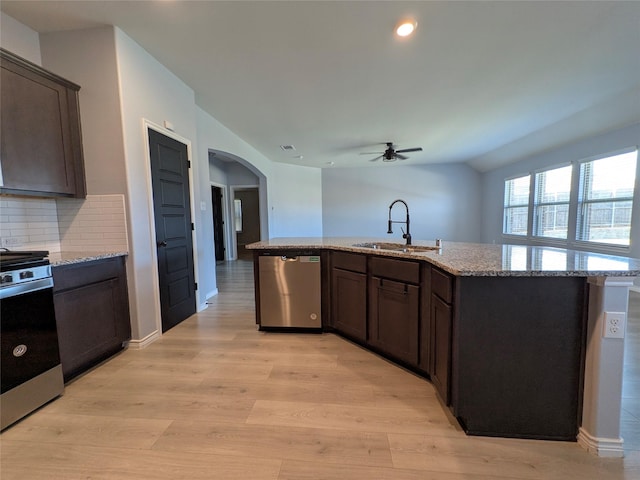 kitchen with arched walkways, stainless steel appliances, light wood-style flooring, a sink, and dark brown cabinets