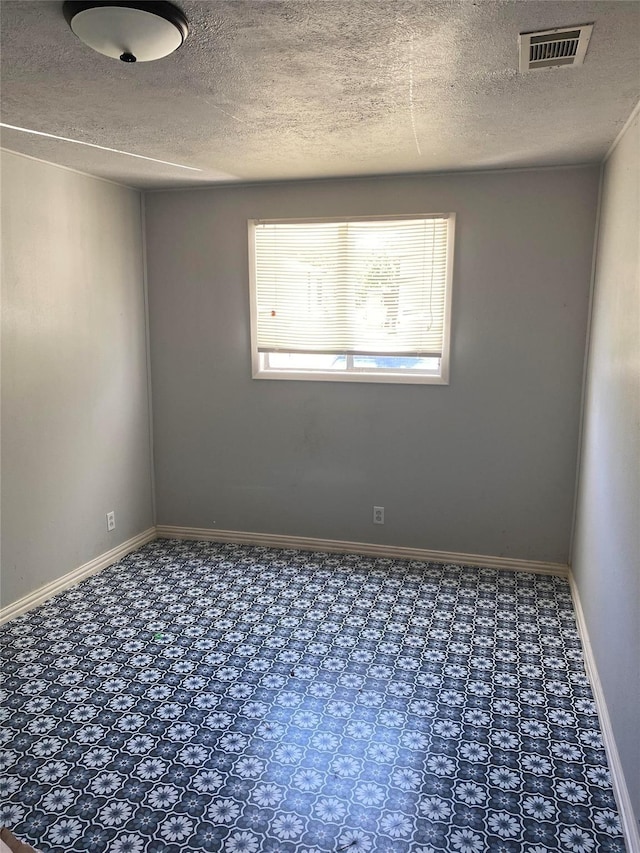 spare room featuring visible vents, a textured ceiling, and baseboards