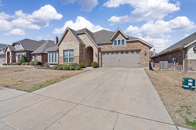 view of front of house with driveway, a garage, stone siding, central AC, and brick siding