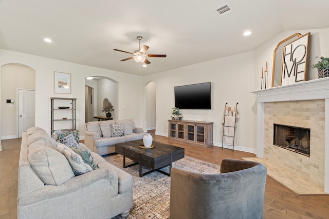 living room featuring arched walkways, visible vents, a fireplace, and wood finished floors