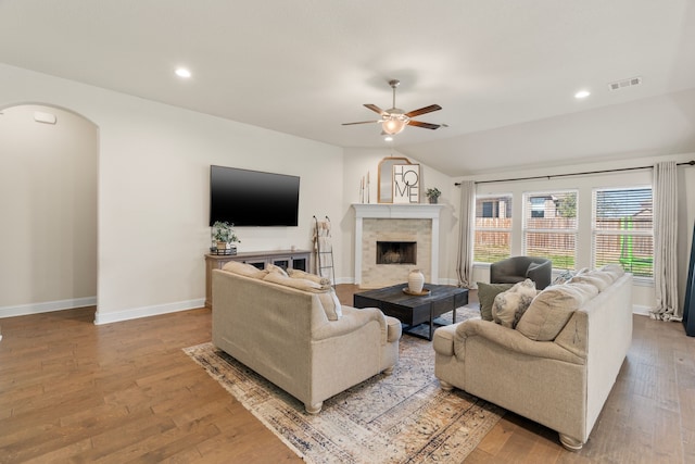 living area featuring arched walkways, ceiling fan, hardwood / wood-style flooring, a fireplace, and visible vents