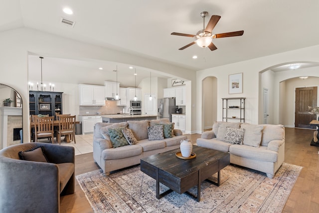 living room with light wood-type flooring, recessed lighting, arched walkways, and ceiling fan with notable chandelier