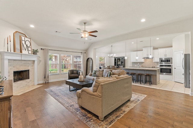 living area with lofted ceiling, light wood-type flooring, a fireplace, and visible vents