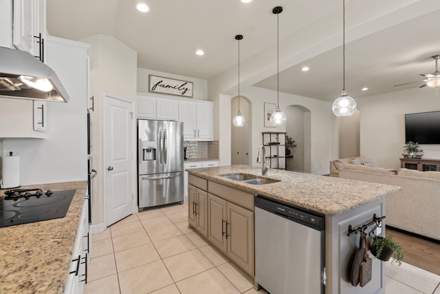 kitchen featuring arched walkways, open floor plan, stainless steel appliances, under cabinet range hood, and a sink