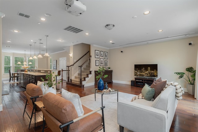 living room with dark wood-style flooring, visible vents, crown molding, and stairway