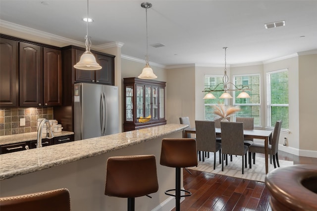 kitchen with dark wood finished floors, backsplash, freestanding refrigerator, dark brown cabinetry, and light stone countertops