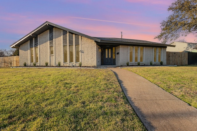 mid-century modern home featuring brick siding, fence, and a front lawn