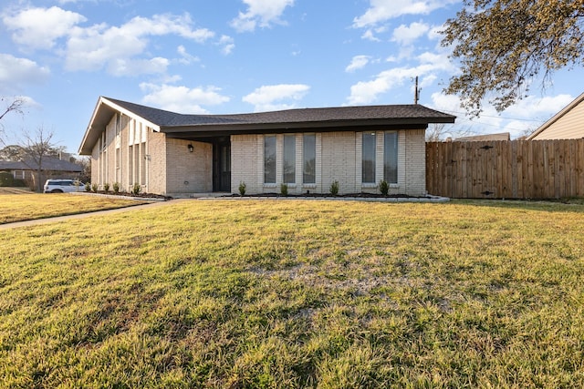 view of front facade featuring brick siding, fence, and a front yard