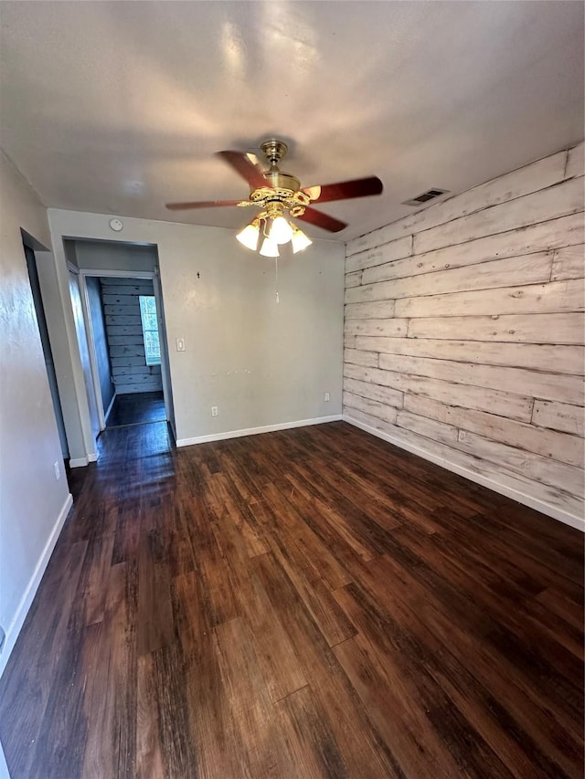 unfurnished room featuring dark wood-type flooring, visible vents, wooden walls, and baseboards