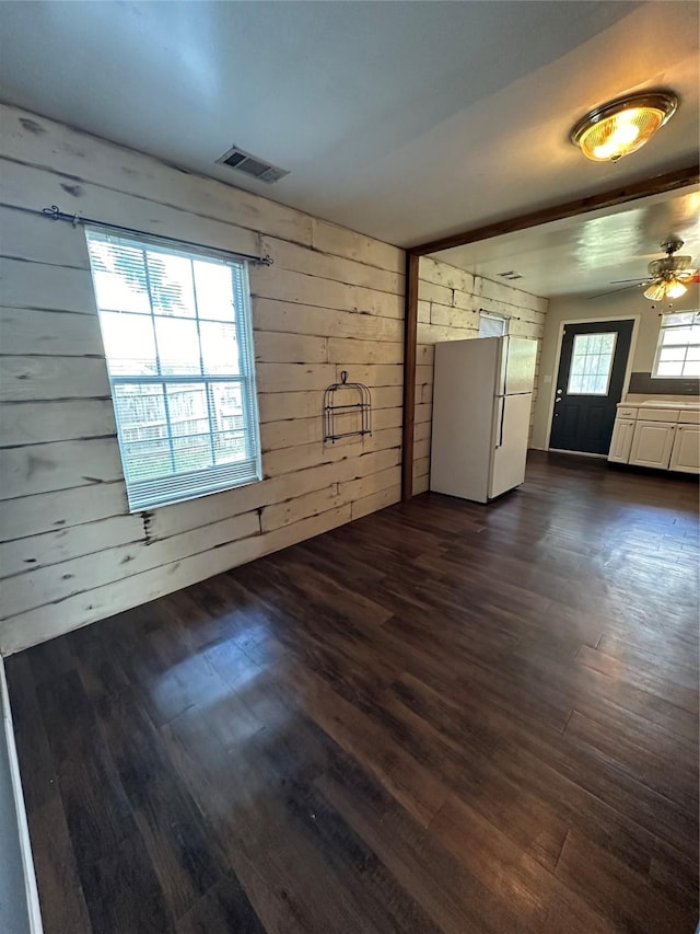 unfurnished room featuring a ceiling fan, dark wood-style flooring, visible vents, and wood walls