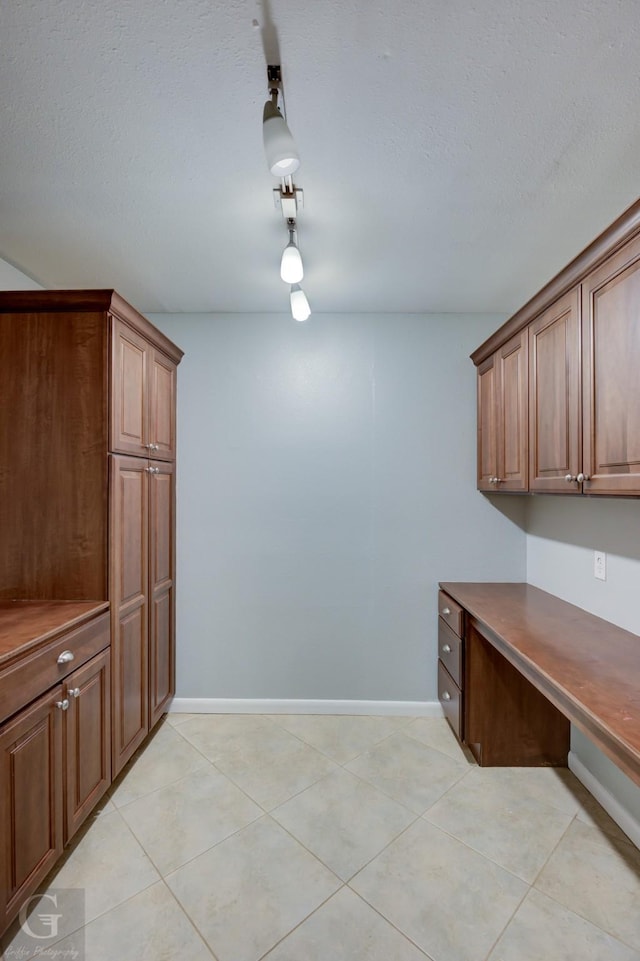 interior space with light tile patterned floors, a textured ceiling, and baseboards