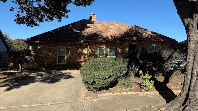 tudor-style house with a tiled roof, brick siding, and a chimney