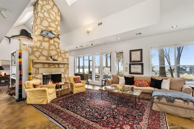 living room featuring high vaulted ceiling, a stone fireplace, a skylight, and a wealth of natural light