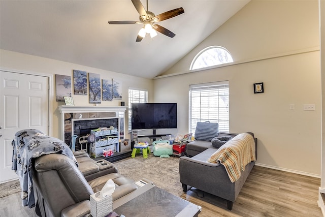 living area featuring high vaulted ceiling, a fireplace, wood finished floors, a ceiling fan, and baseboards