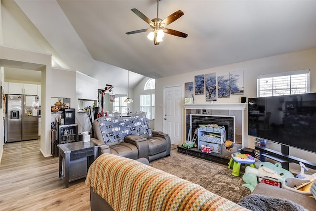 living room featuring light wood-type flooring, lofted ceiling, a fireplace, and a ceiling fan