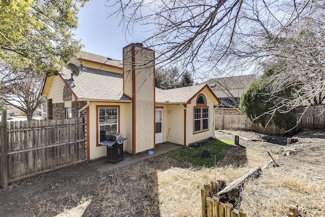 rear view of house featuring a fenced backyard, a chimney, and a shingled roof