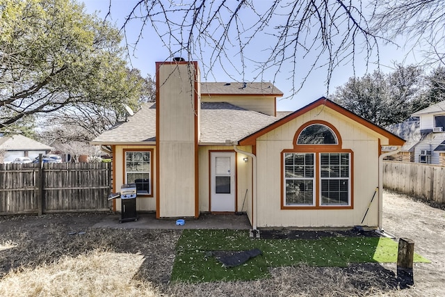 rear view of house featuring fence private yard, a shingled roof, and a chimney