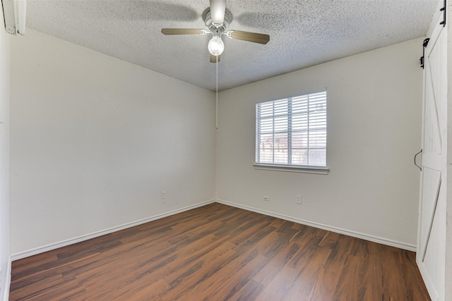 spare room with a barn door, baseboards, a ceiling fan, dark wood-style flooring, and a textured ceiling