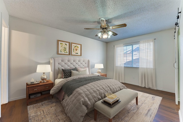 bedroom with dark wood finished floors, a textured ceiling, baseboards, and a barn door