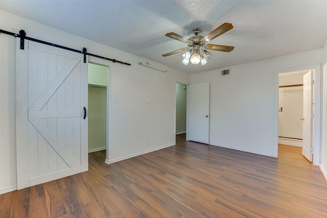 unfurnished bedroom featuring wood finished floors, visible vents, a spacious closet, and a barn door