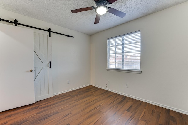 empty room with a barn door, baseboards, a ceiling fan, wood finished floors, and a textured ceiling