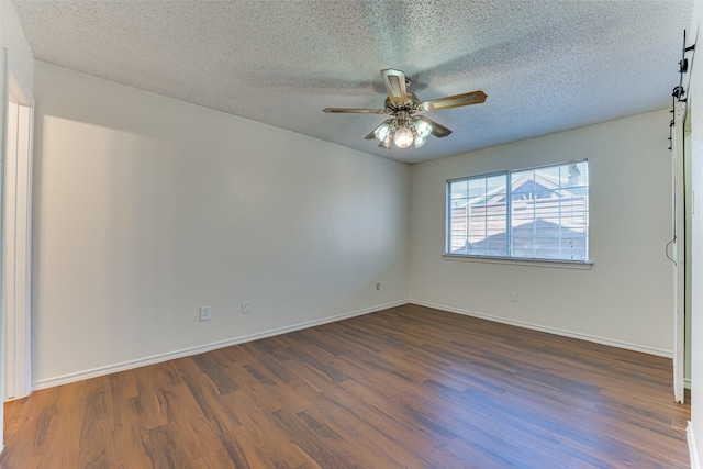 spare room featuring a barn door, wood finished floors, a ceiling fan, and baseboards