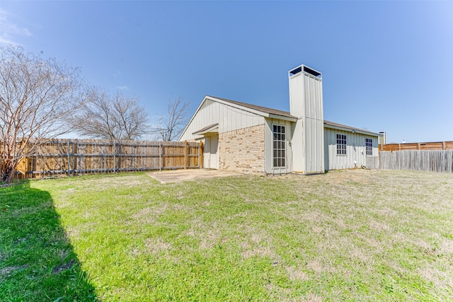 rear view of property featuring a lawn, a fenced backyard, a chimney, a patio area, and brick siding