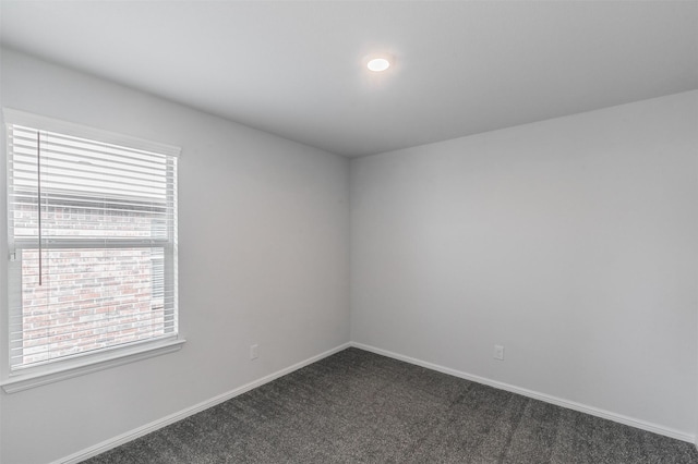 spare room featuring baseboards and dark carpet