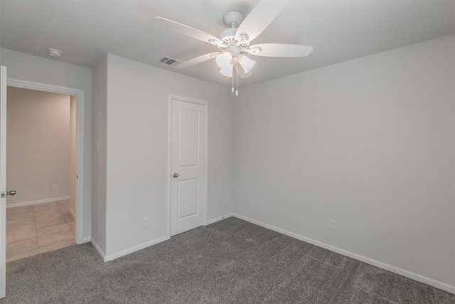 spare room featuring a ceiling fan, dark colored carpet, visible vents, and baseboards