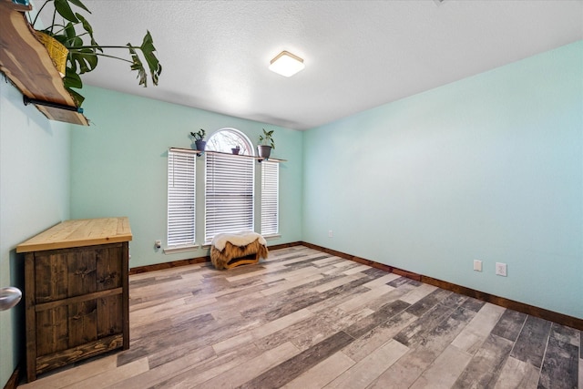 empty room with a textured ceiling, baseboards, and wood finished floors