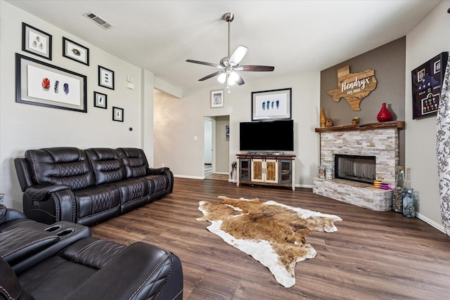 living room featuring visible vents, a ceiling fan, a stone fireplace, wood finished floors, and baseboards