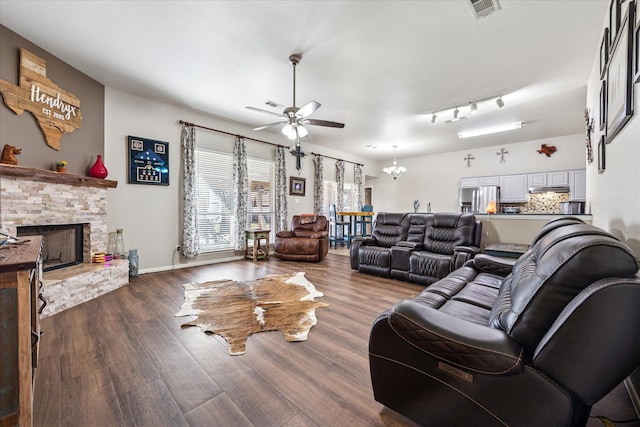 living room featuring dark wood-style floors, a stone fireplace, ceiling fan with notable chandelier, and visible vents