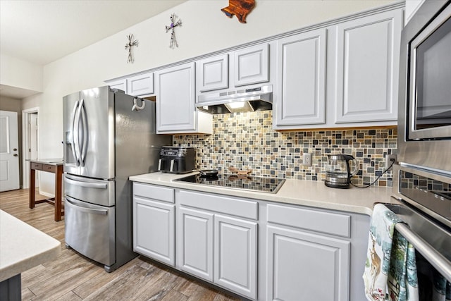 kitchen with under cabinet range hood, stainless steel appliances, light countertops, light wood-type flooring, and tasteful backsplash