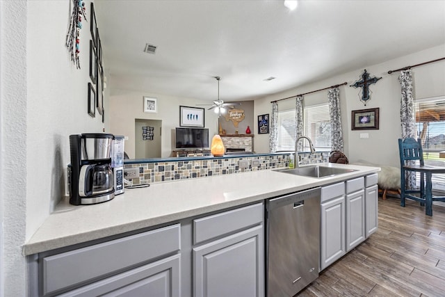 kitchen featuring backsplash, a sink, a stone fireplace, wood finished floors, and dishwasher