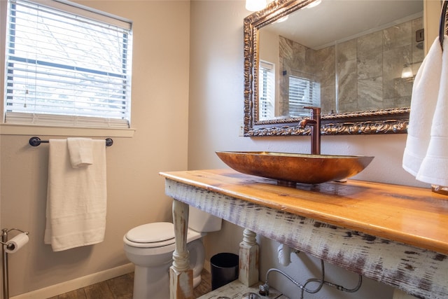 bathroom featuring toilet, wood finished floors, a sink, baseboards, and tiled shower