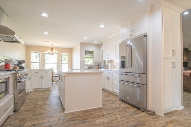 kitchen with wall chimney exhaust hood, a kitchen island, high quality appliances, and white cabinets