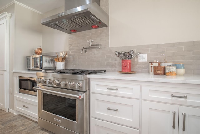 kitchen with tasteful backsplash, light countertops, appliances with stainless steel finishes, white cabinetry, and ventilation hood