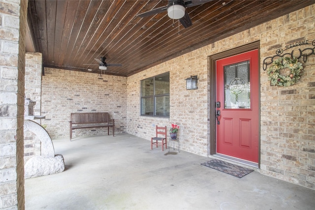 view of exterior entry with brick siding, a patio area, and a ceiling fan