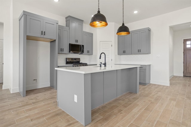 kitchen with wood finish floors, stainless steel appliances, tasteful backsplash, gray cabinets, and light countertops