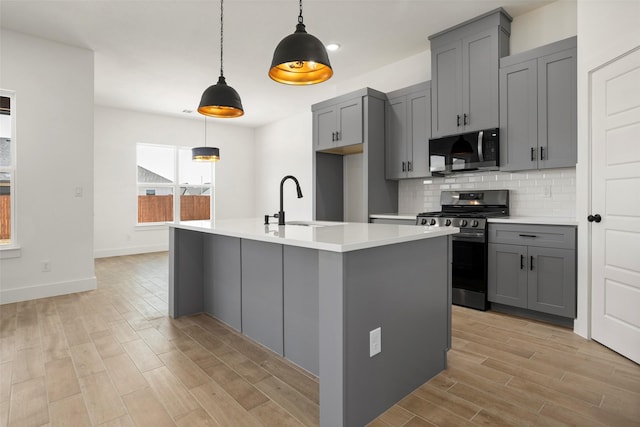 kitchen with gray cabinetry, backsplash, stainless steel appliances, wood finish floors, and a sink