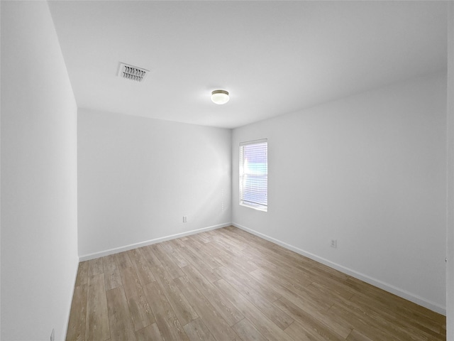 spare room featuring light wood-type flooring, visible vents, and baseboards