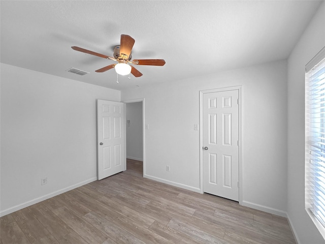 unfurnished bedroom featuring baseboards, a ceiling fan, visible vents, and light wood-style floors