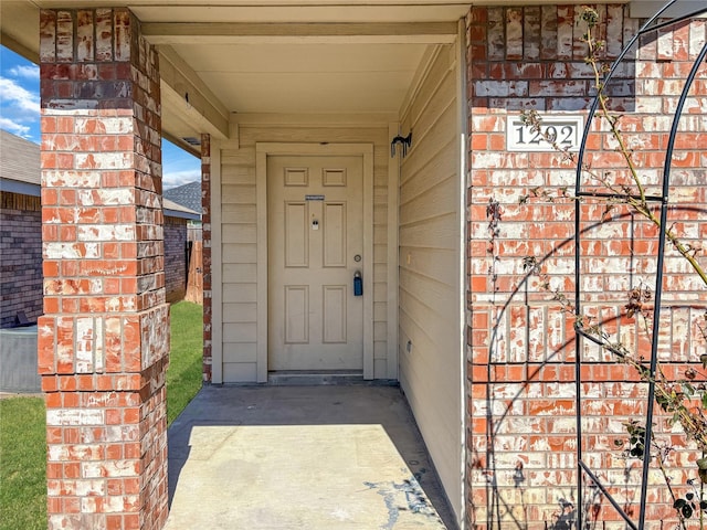 view of exterior entry featuring central AC and brick siding