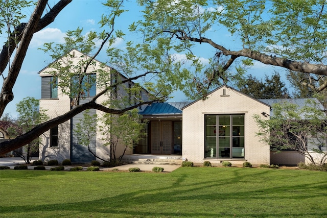 view of front of home featuring metal roof, brick siding, a standing seam roof, and a front lawn